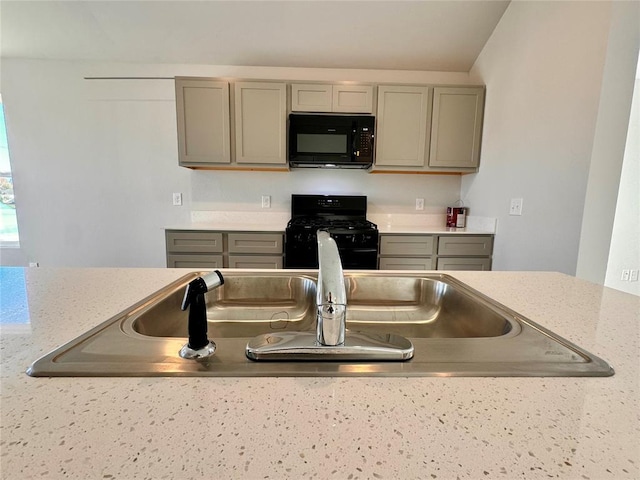 kitchen with sink, light stone counters, gray cabinetry, and black appliances