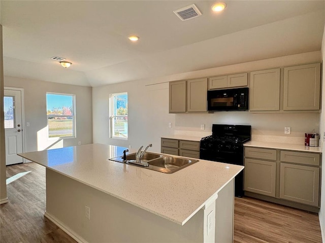 kitchen with hardwood / wood-style floors, sink, an island with sink, and black appliances