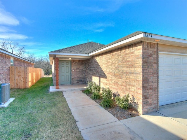 entrance to property featuring a lawn, cooling unit, and a garage