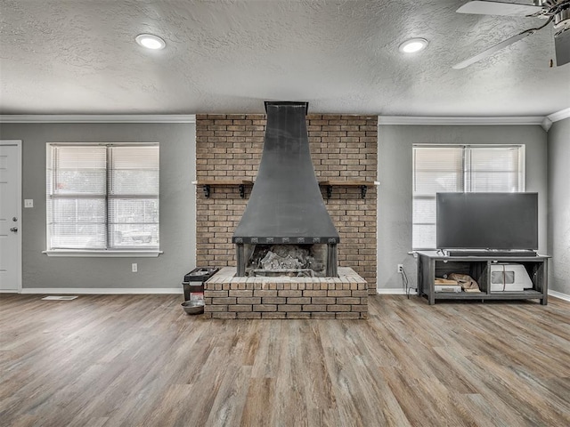 unfurnished living room featuring hardwood / wood-style floors, crown molding, a wood stove, and a textured ceiling