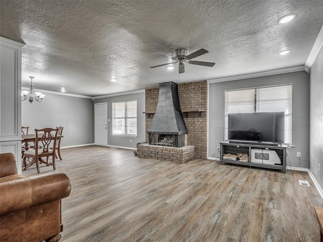 living room with a wood stove, ceiling fan with notable chandelier, crown molding, a textured ceiling, and wood-type flooring