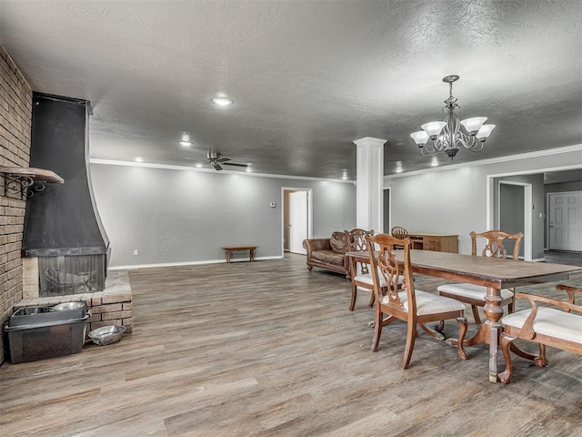 dining space featuring ceiling fan with notable chandelier, light hardwood / wood-style floors, crown molding, and a brick fireplace