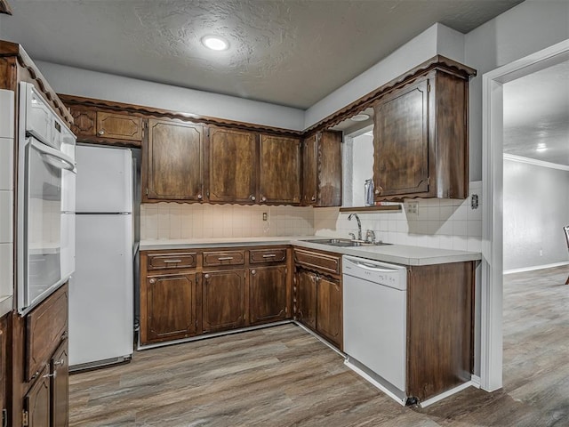 kitchen with dark brown cabinetry, white appliances, sink, and light wood-type flooring