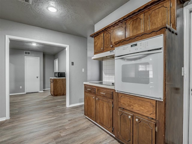 kitchen featuring white oven, black electric stovetop, light hardwood / wood-style flooring, a textured ceiling, and tasteful backsplash