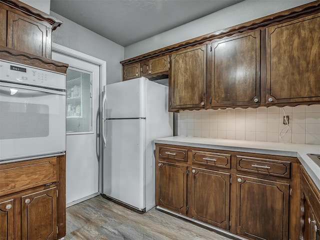 kitchen featuring dark brown cabinets, light wood-type flooring, white appliances, and tasteful backsplash