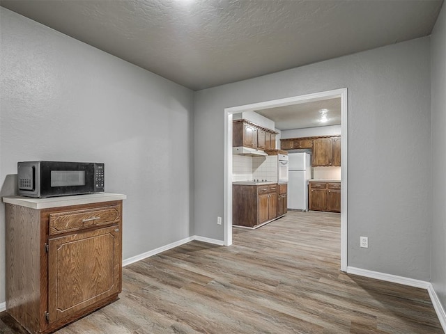 kitchen with a textured ceiling, white refrigerator, light wood-type flooring, and backsplash