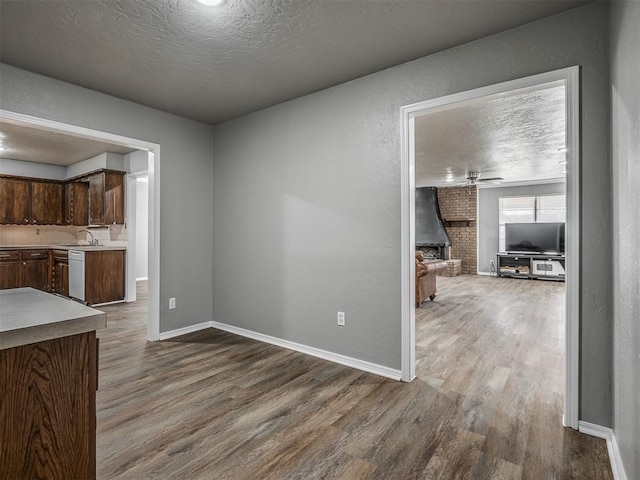 interior space with white dishwasher, ceiling fan, a textured ceiling, dark brown cabinets, and wood-type flooring