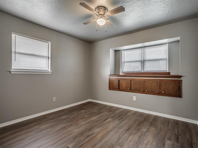 empty room featuring a textured ceiling, plenty of natural light, dark wood-type flooring, and ceiling fan