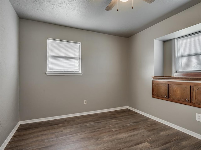 unfurnished room featuring a wealth of natural light, ceiling fan, dark wood-type flooring, and a textured ceiling