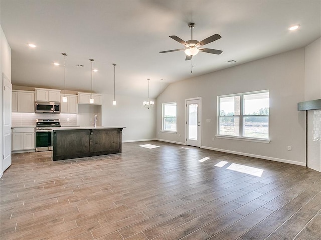 kitchen with ceiling fan with notable chandelier, stainless steel appliances, pendant lighting, white cabinetry, and an island with sink