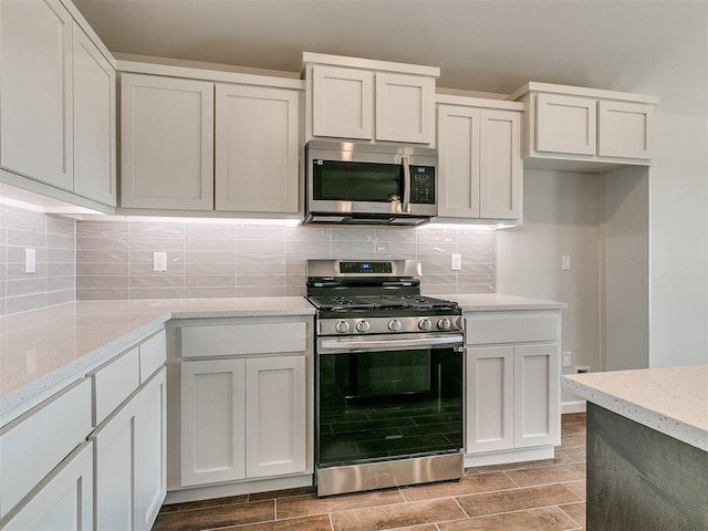 kitchen featuring tasteful backsplash, light stone countertops, white cabinets, and stainless steel appliances