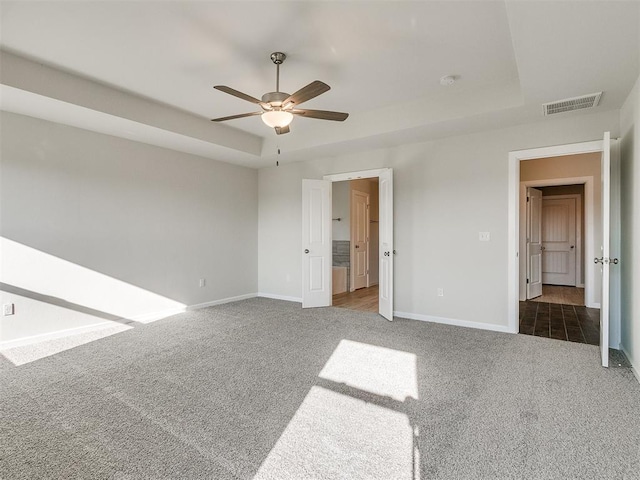 unfurnished bedroom with ceiling fan, dark carpet, and a tray ceiling