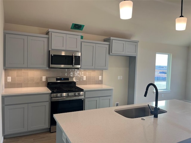 kitchen with pendant lighting, sink, decorative backsplash, light stone countertops, and stainless steel appliances