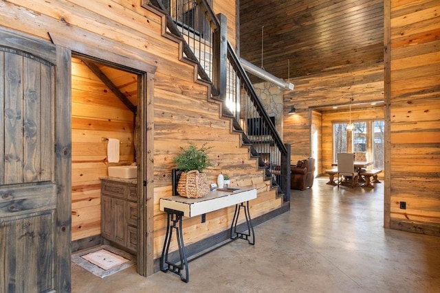 interior space featuring an inviting chandelier, concrete floors, wooden walls, and high vaulted ceiling