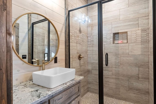 bathroom featuring a shower with shower door, wood walls, and vanity