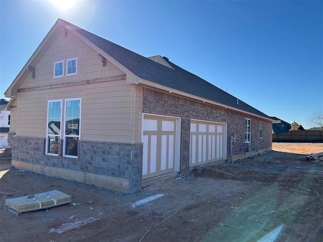 view of side of home with an attached garage, a shingled roof, and fence