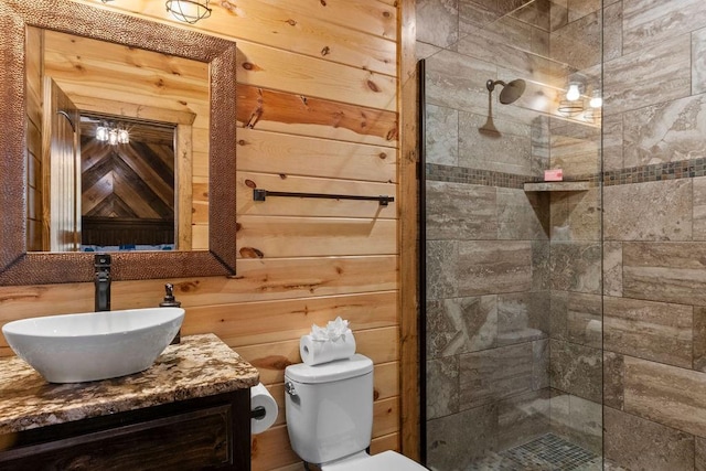 bathroom with toilet, vanity, wooden walls, and tiled shower