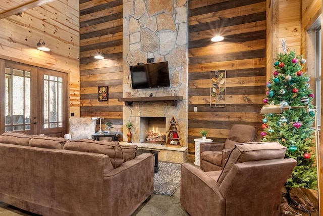 living room with a high ceiling, french doors, a stone fireplace, and wooden walls