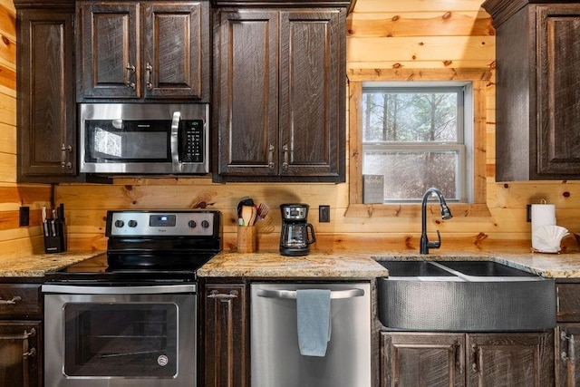 kitchen featuring appliances with stainless steel finishes, dark brown cabinetry, wooden walls, and sink