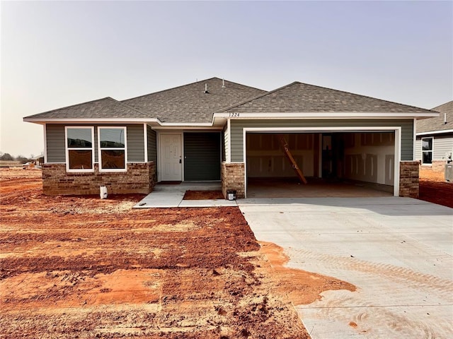 prairie-style home featuring an attached garage, brick siding, driveway, and a shingled roof