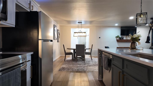 kitchen featuring gray cabinets, appliances with stainless steel finishes, wood-type flooring, and decorative light fixtures