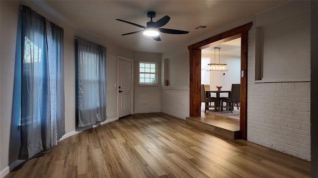 unfurnished room featuring brick wall, ceiling fan with notable chandelier, and hardwood / wood-style flooring