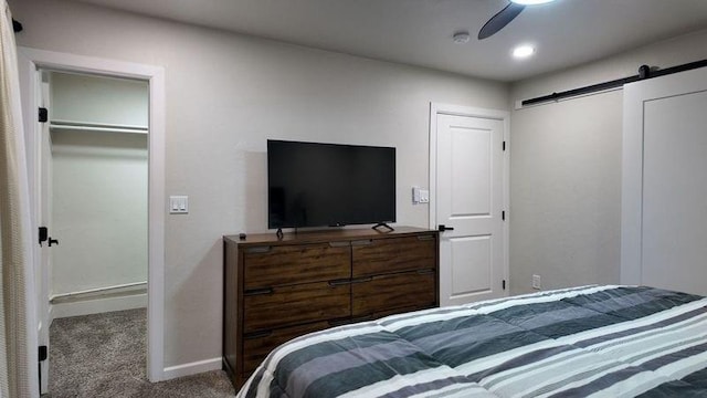 bedroom featuring ceiling fan, a barn door, and dark colored carpet