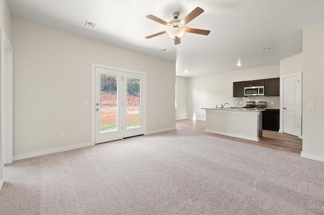 unfurnished living room with ceiling fan, sink, and light carpet