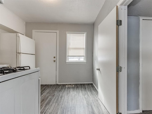 kitchen featuring hardwood / wood-style flooring, white appliances, white cabinets, and a textured ceiling