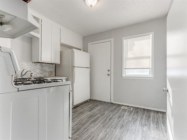 kitchen with white cabinetry, light hardwood / wood-style floors, backsplash, and white appliances