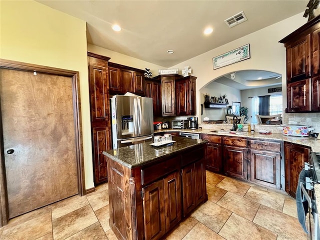 kitchen featuring a center island, dark brown cabinets, dark stone counters, and appliances with stainless steel finishes