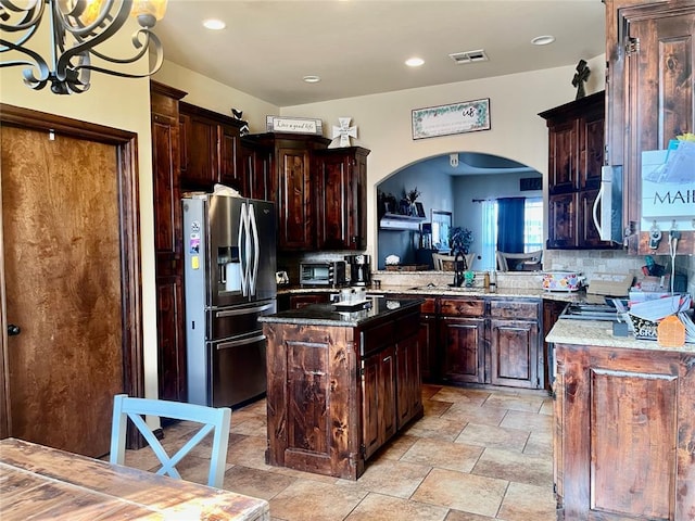 kitchen with decorative light fixtures, decorative backsplash, dark stone counters, a kitchen island, and appliances with stainless steel finishes