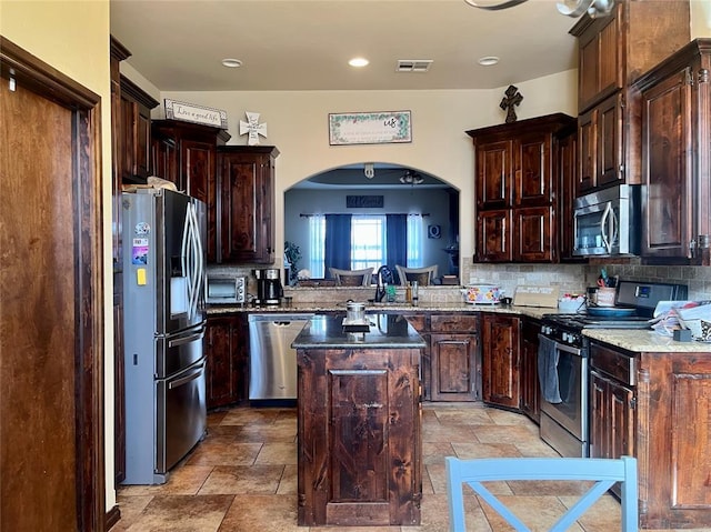 kitchen featuring appliances with stainless steel finishes, a center island, dark brown cabinetry, sink, and tasteful backsplash