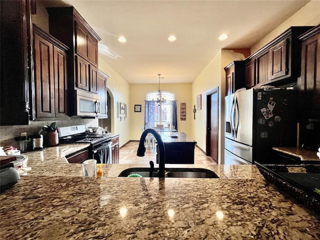 kitchen with sink, decorative light fixtures, an inviting chandelier, light stone countertops, and appliances with stainless steel finishes