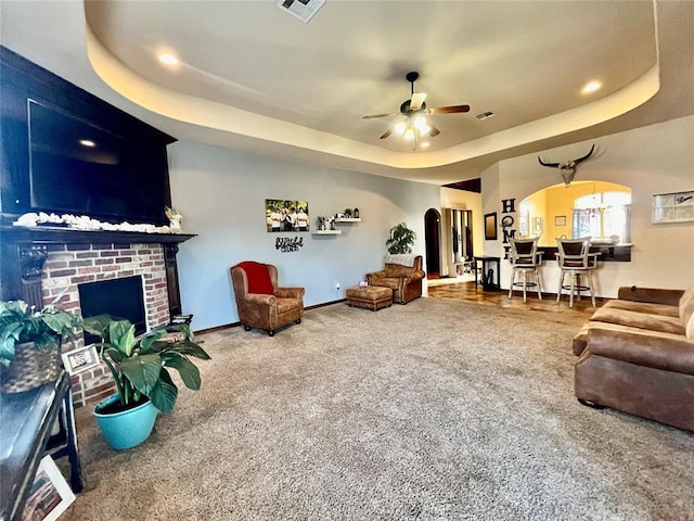 living room with ceiling fan, a raised ceiling, carpet floors, and a fireplace