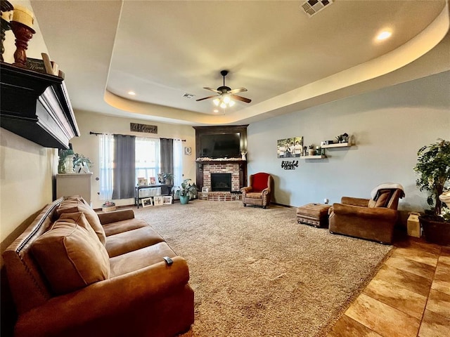 living room with ceiling fan, a fireplace, and a tray ceiling