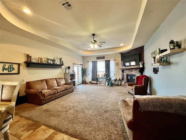 carpeted living room featuring a fireplace, ceiling fan, and a tray ceiling