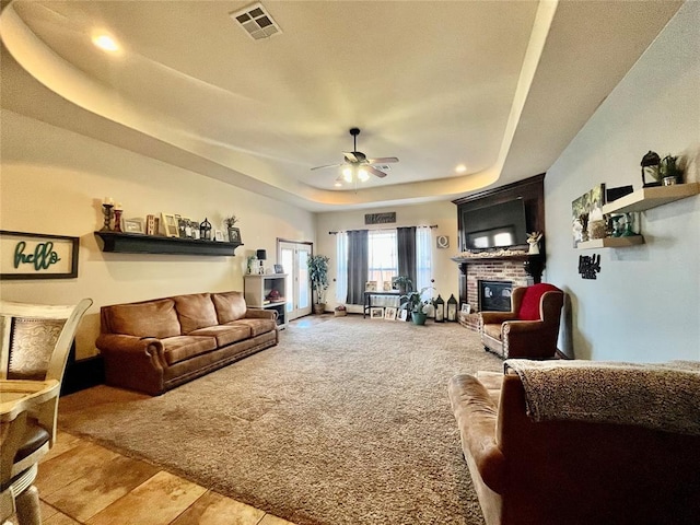 living room with a fireplace, a raised ceiling, ceiling fan, and light carpet