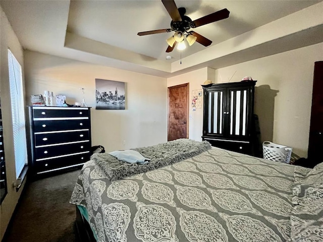 carpeted bedroom featuring ceiling fan and a tray ceiling