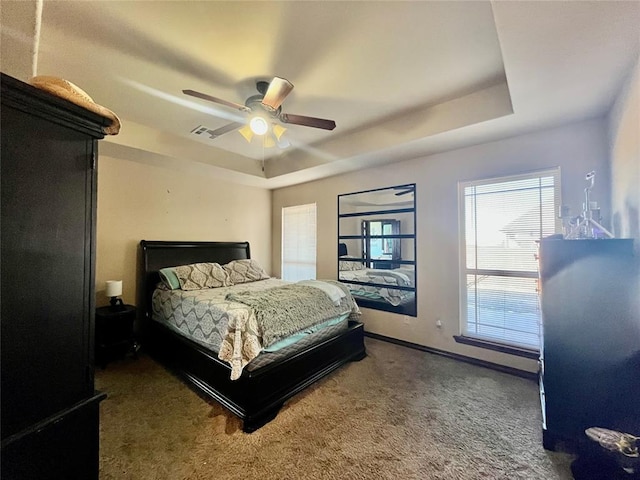 carpeted bedroom with a raised ceiling and ceiling fan