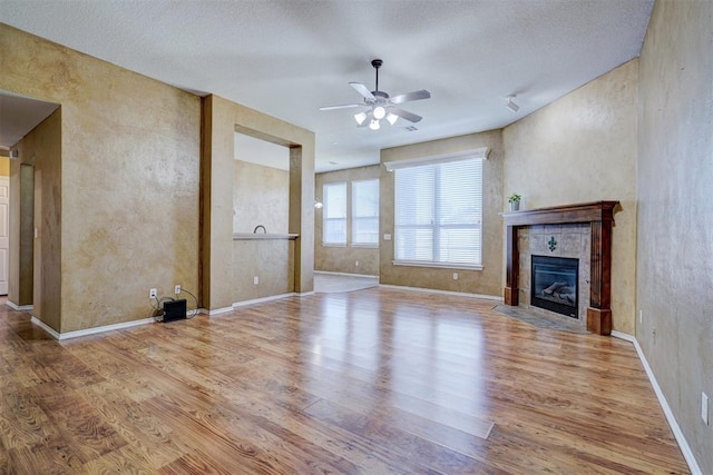 unfurnished living room featuring a tiled fireplace, ceiling fan, and light wood-type flooring