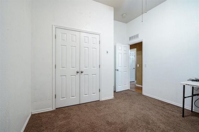 unfurnished bedroom featuring a towering ceiling, a closet, and dark colored carpet