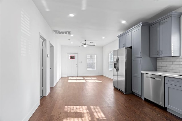 kitchen featuring gray cabinetry, dark wood-type flooring, ceiling fan, appliances with stainless steel finishes, and tasteful backsplash