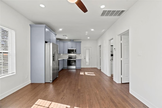 kitchen featuring ceiling fan, decorative backsplash, gray cabinets, appliances with stainless steel finishes, and dark hardwood / wood-style flooring