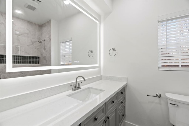 bathroom featuring a tile shower, plenty of natural light, vanity, and toilet