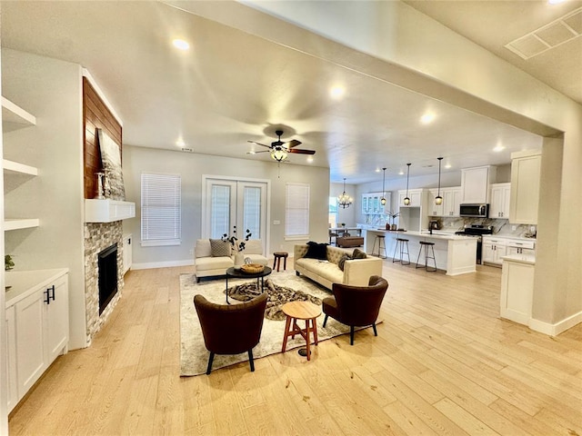 living room featuring french doors, a fireplace, ceiling fan, and light hardwood / wood-style flooring