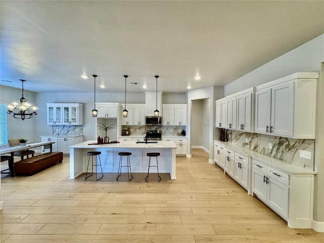 kitchen featuring hanging light fixtures, an island with sink, stainless steel appliances, a notable chandelier, and white cabinetry