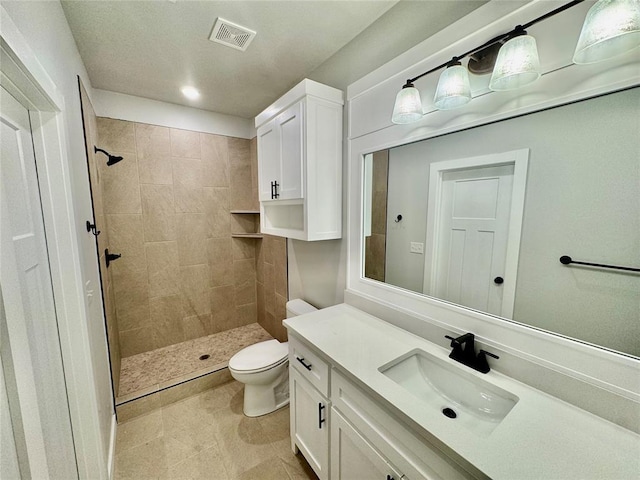 bathroom with toilet, a tile shower, and vanity