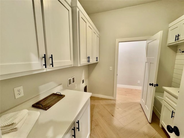 clothes washing area with electric dryer hookup, light wood-type flooring, cabinets, and washer hookup