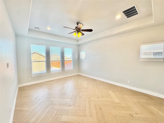 unfurnished room with light parquet flooring, a raised ceiling, and ceiling fan